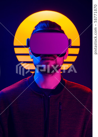 VR head set videogame in 80's synth wave and retro wave futuristic aesthetics. Man wearing virtual reality goggles looking straight. 58771870