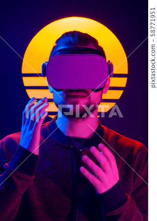 Man wearing virtual reality goggles and interacts with hand gestures. VR head set videogame in 80's synthwave and retrowave futuristic aesthetics. 58771951