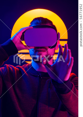 Man wearing virtual reality glasses headset. Vr world experience. Videogame in 80's synthwave and retrowave futuristic aesthetics. 58771952