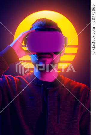 VR head set videogame in 80's synthwave and retrowave futuristic vaporwave aesthetics. Man wearing virtual reality goggles retro vaporwave neon style. 58772069