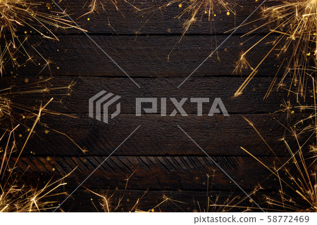Festive burning sparklers with sparks background. Burning bengal fire with glitter particles over wooden background. Festive burning sparklers with sparks background. Burning bengal fire with glitter particles over wooden background. 58772469