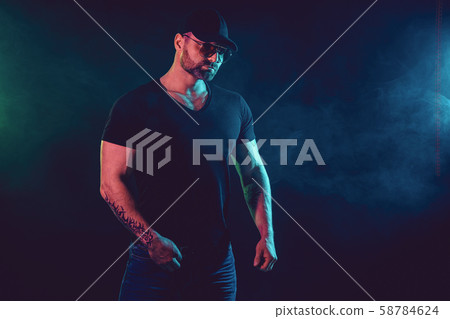 Young strong man bodybuilder in cap on wall background. Dark dramatic colors. 58784624