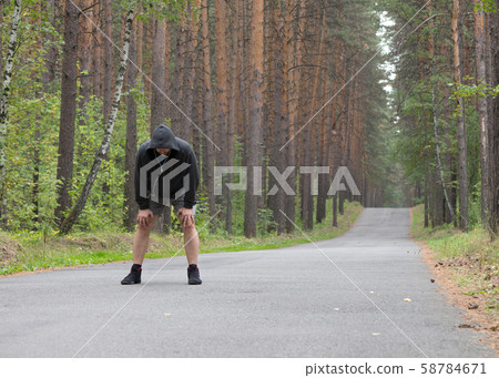 Tired man in grey hoodie making a stop after jogging on road in the forest, selective focus 58784671
