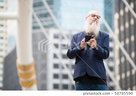 Mature bearded bald businessman thinking while using phone in the city outdoors 58785590