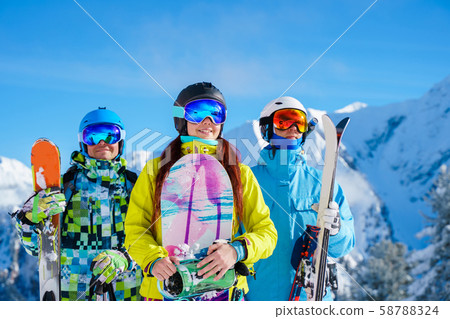 Happy man and woman with snowboard and skis standing on snow resort against backdrop of mountain in 58788324