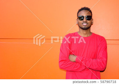 Happy young African bearded man smiling with arms crossed against orange wall 58790718