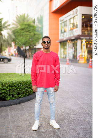 Full body shot of happy young African man smiling with sunglasses at the city streets 58790750