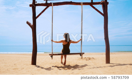 Young woman in swimsuit is riding on a swing on the beach 58793709