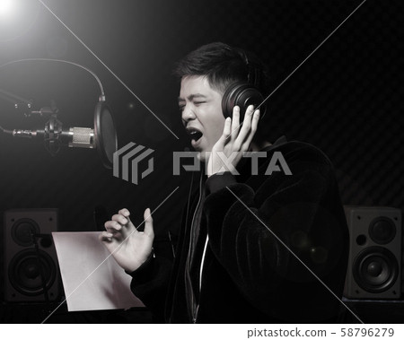 Asian Teenager man black hair earmuff headphone sing a song loudly power sound over hanging microphone condenser, speakers, composer note book and monitor. Studio Sound Proof Absorbing wall room 58796279
