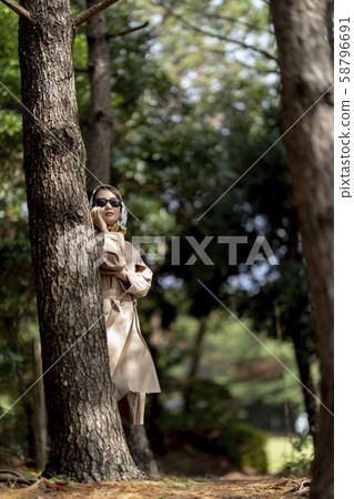 一名穿著風衣的女人躲在防風林中，有懸疑劇，並在智能手機上與朋友秘密交談 58796691