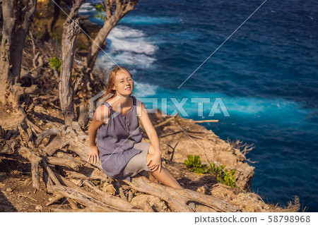 Woman sitting on a tree against the background of the sea Angel's Billabong in Nusa Penida, Bali Woman sitting on a tree against the background of the sea Angel's Billabong in Nusa Penida, Bali 58798968