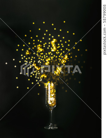 Golden star shaped confetti and party streamers poured out of champagne glass on black background Golden star shaped confetti and party streamers poured out of champagne glass on black background 58799008