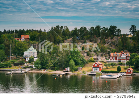 Sweden. Beautiful Red Swedish Wooden Log Cabin House On Rocky Island Coast In Summer Sunny Evening Sweden. Beautiful Red Swedish Wooden Log Cabin House On Rocky Island Coast In Summer Sunny Evening 58799642