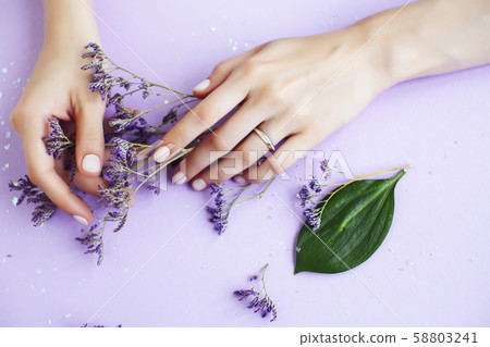 pretty perfect woman hands with white manicure and little flowers on colorful lilac background 58803241