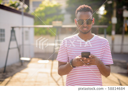 Happy young African bearded man with sunglasses using phone outdoors 58814684