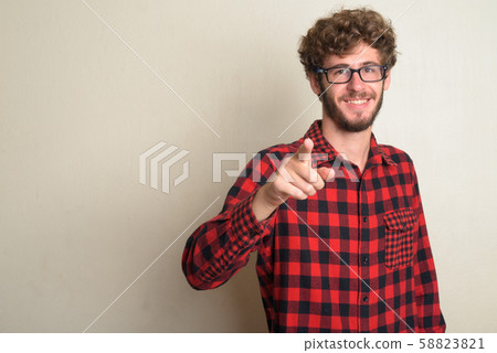 Happy young bearded hipster man with curly hair pointing at camera 58823821