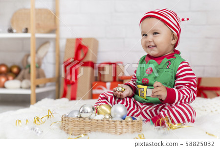 Sweet baby in elf costume playing with Christmas decorations Sweet baby in elf costume playing with Christmas decorations 58825032