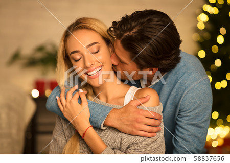 Man kissing neck of stunning woman sitting near Christmas tree 58837656