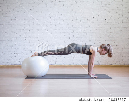 Caucasian woman doing plank position using math and fitness ball, loft background, toned blue Caucasian woman doing plank position using math and fitness ball, loft background, toned blue 58838217