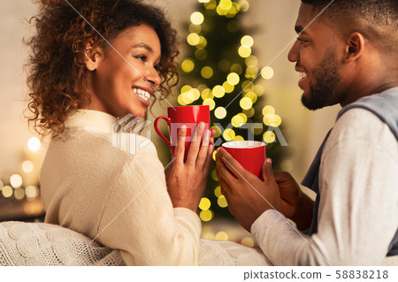 Loving african-american couple drinking tea against Christmas tree Loving african-american couple drinking tea against Christmas tree 58838218