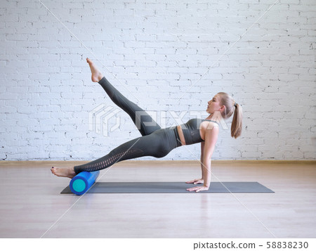 Caucasian young woman in grey sports suit doing pilates workout on math with fitness roller, loft 58838230