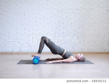 Gluteal bridge on foam roller. Young caucasian woman doing pilates with special equipment in fitness 58838231