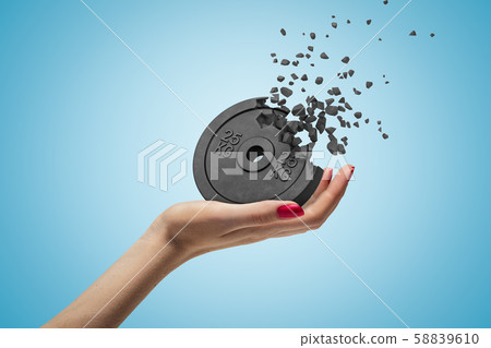 Side closeup of woman's hand facing up and holding black 25kg weight plate that is dissolving in 58839610