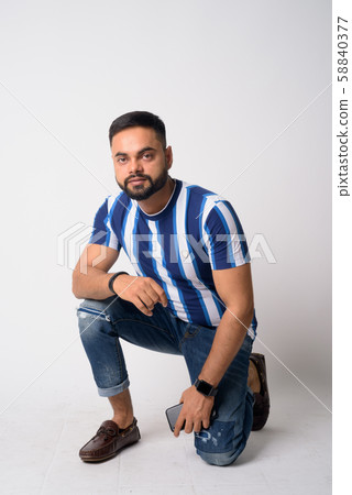 Full body shot of young bearded Indian man crouching 58840377
