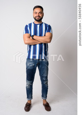 Full body shot of happy young bearded Indian man smiling with arms crossed Full body shot of happy young bearded Indian man smiling with arms crossed 58840456