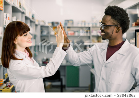 Two happy colleages pharmacists, African man and Caucasian woman working in drugstore, smiling 58842862