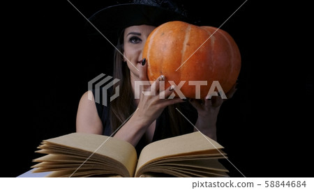Beautiful sexy woman in a black witch costume and hat holding a pumpkin. Halloween holiday party Beautiful sexy woman in a black witch costume and hat holding a pumpkin. Halloween holiday party 58844684