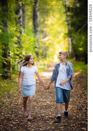 First love. Little boy and girl holding hands and smiling while walking outdoors in park 58844826
