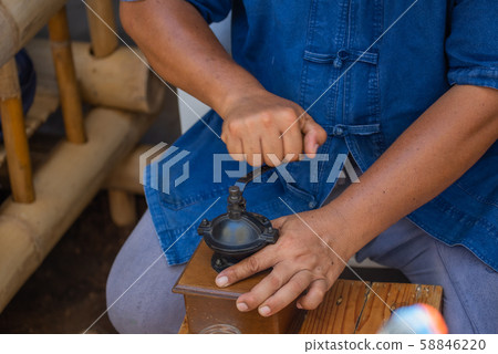 • Man grinds with an old coffee mill with crank fresh coffee powder for coffee. • Man grinds with an old coffee mill with crank fresh coffee powder for coffee. 58846220