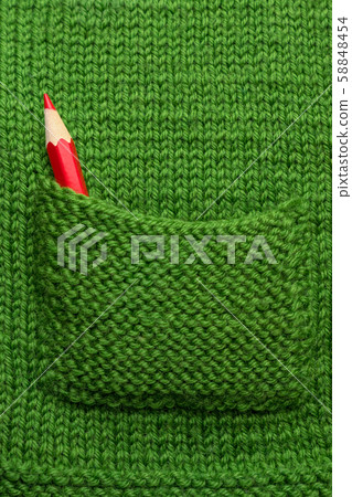 Knitting background. Red crayon in green knitted pocket. Part of clothing. Sweater, jacket, handmade 58848454