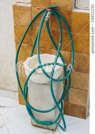 Old wall tap with a coiled green hosepipe Old wall tap with a coiled green hosepipe 58852250