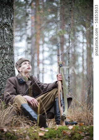 A soldier of World War II is sitting near the tree and looking up 58853633