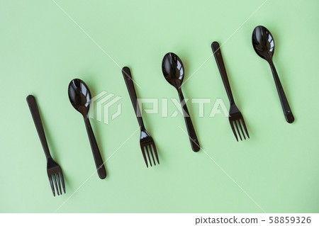 Black plastic spoons and forks lay on a green background in neo light Black plastic spoons and forks lay on a green background in neo light 58859326