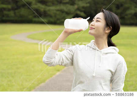 Woman drinking protein in a grassy park Woman drinking protein in a grassy park 58863186
