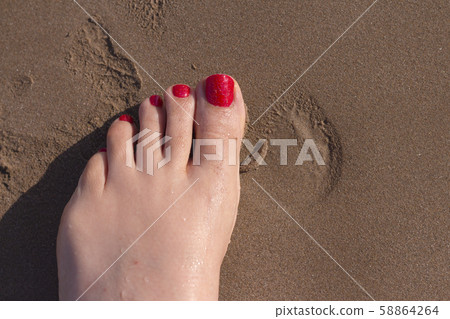 Feet of woman with nails painted red on the sand Feet of woman with nails painted red on the sand 58864264