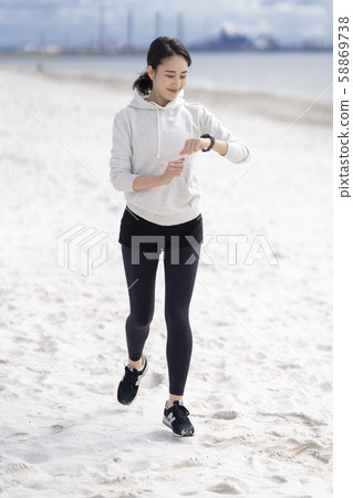 Woman running on sandy beach taking care of time Woman running on sandy beach taking care of time 58869738