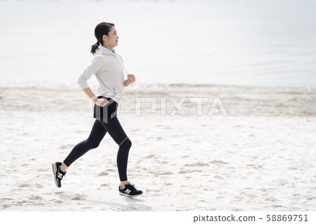 Woman running while taking the morning sun on a white sand beach 58869751