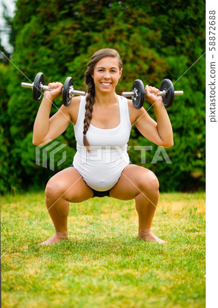 Pregnant Woman Doing Squat Press Using Weights In Park 58872688