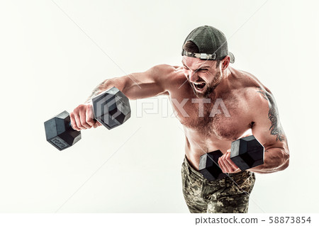 Muscular athlete bodybuilder man in camouflage pants with a naked torso punching with dumbbells like 58873854