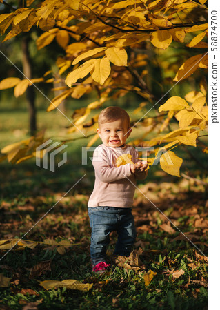 Cute baby girl stand about beautiful yellow tree and play with leaf on the tree 58874700