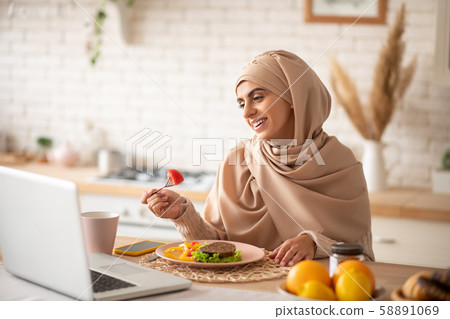 Muslim girl enjoying a dinner while watching videos on her laptop Muslim girl enjoying a dinner while watching videos on her laptop 58891069