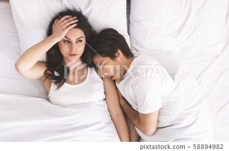 Grumpy woman with insomnia lying with man in bed Grumpy woman with insomnia lying with man in bed 58894982
