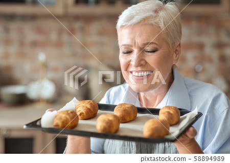 Portrait of old woman presenting tray with self made croissants Portrait of old woman presenting tray with self made croissants 58894989