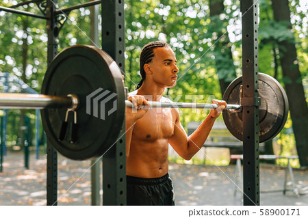 Young man leaning over weight bar after training outdoors Young man leaning over weight bar after training outdoors 58900171