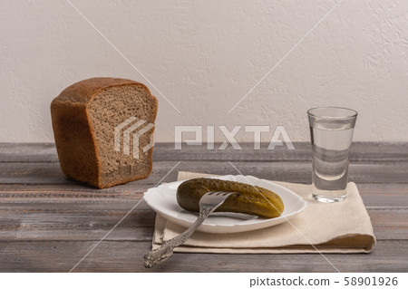 Traditional Russian snack - a glass of vodka with pickles with fork and rye black bread. Rustic Traditional Russian snack - a glass of vodka with pickles with fork and rye black bread. Rustic 58901926