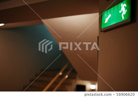 Green escape route sign on a flight of stairs. 58906620